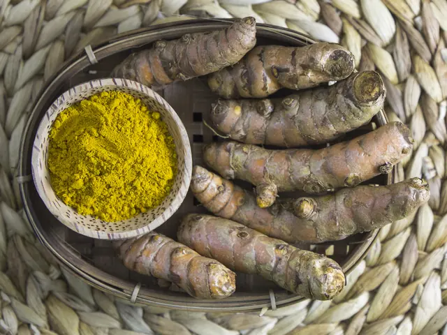 Golden-yellow turmeric powder in a woven bowl beside whole turmeric rhizomes